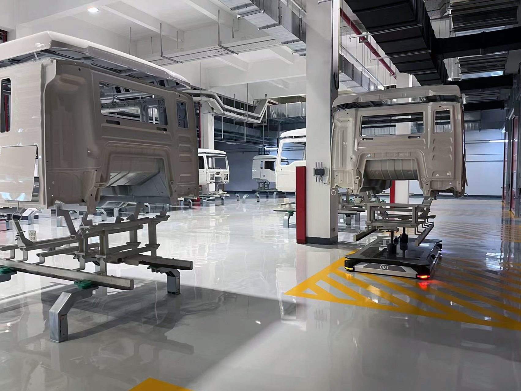 Low-slung AGVs carrying truck cabs in a shiny factory. 